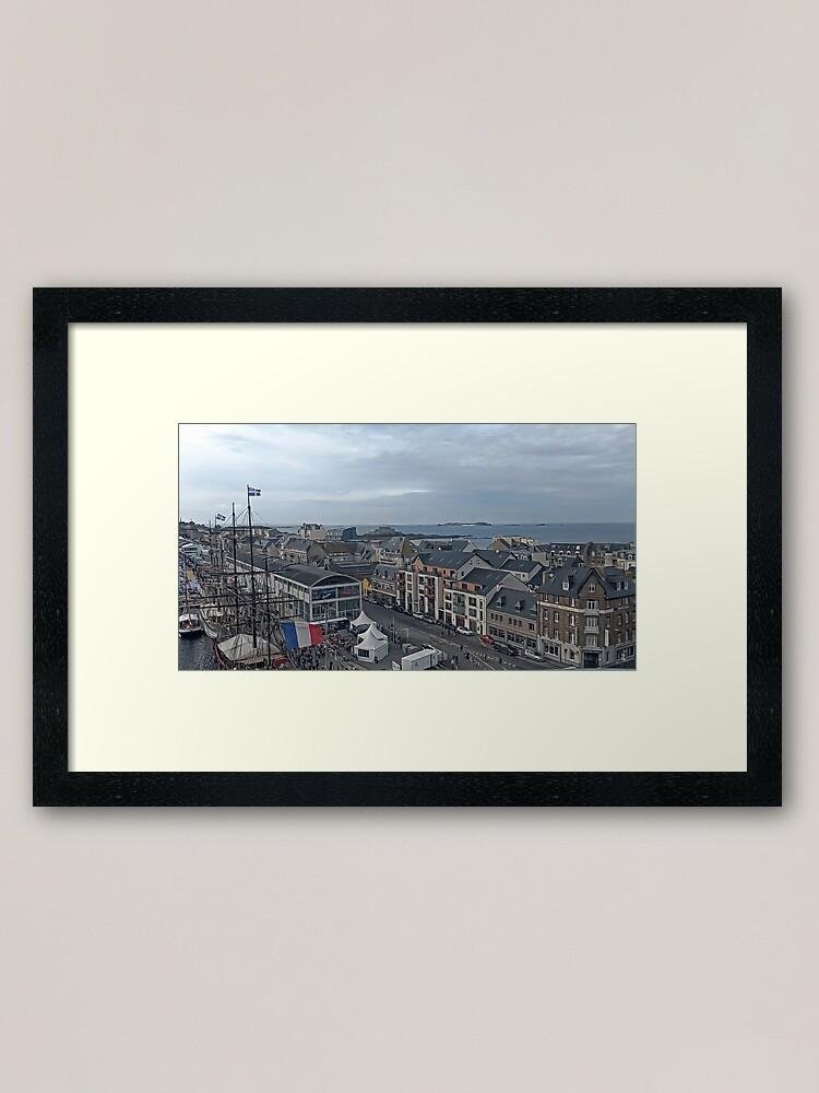 Panoramic view over the port of Saint-Malo with sailing masts, historic rooftops and the sea horizon under a soft cloudy sky in Brittany, France.