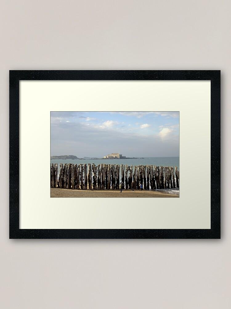 Wooden breakwater posts on Saint-Malo beach with Fort National in the distance under a soft coastal sky.