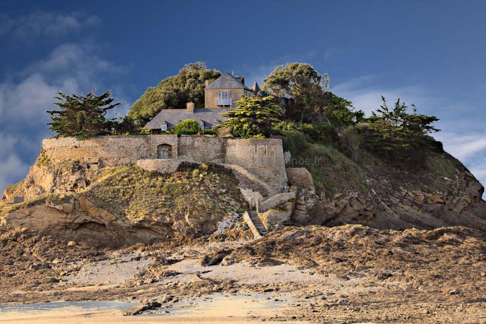 Sunny day view of Fort du Guesclin island in Saint-Malo, France. Bright blue sky over a medieval fortress and rocky beach. Traditional French coastal architecture and emerald sea landscape.