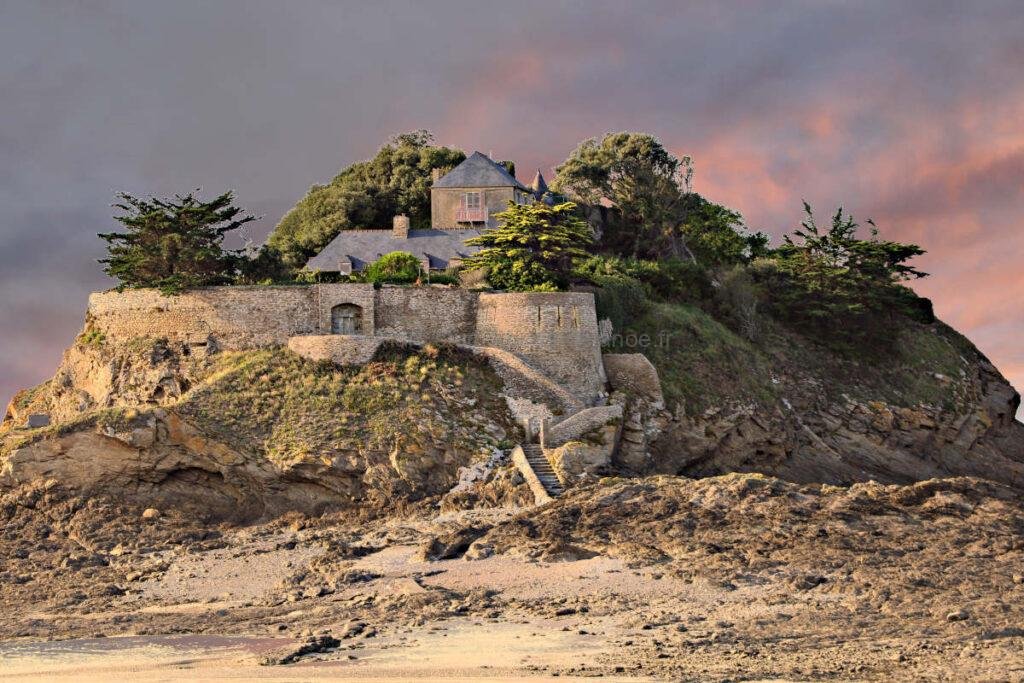 Dramatic sunset over Fort du Guesclin in Brittany, France. A historic island castle glowing under a vibrant orange and pink sky at low tide. Warm coastal landscape photography for home decor.